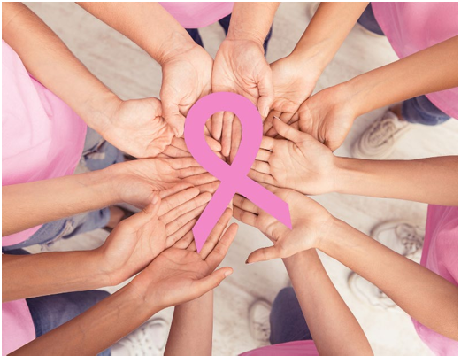 A circle of women't hands holding a giant Breast Cancer Awareness ribbon